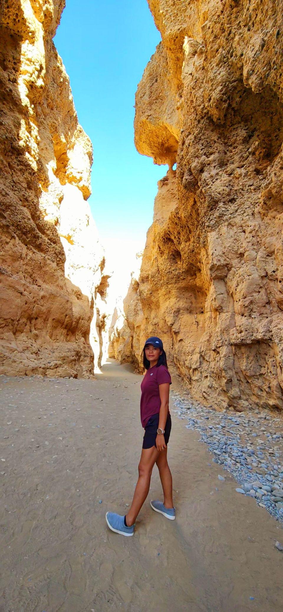 Max walks through the sandy corridor of Sesriem Canyon, sandstone walls rising on both sides.