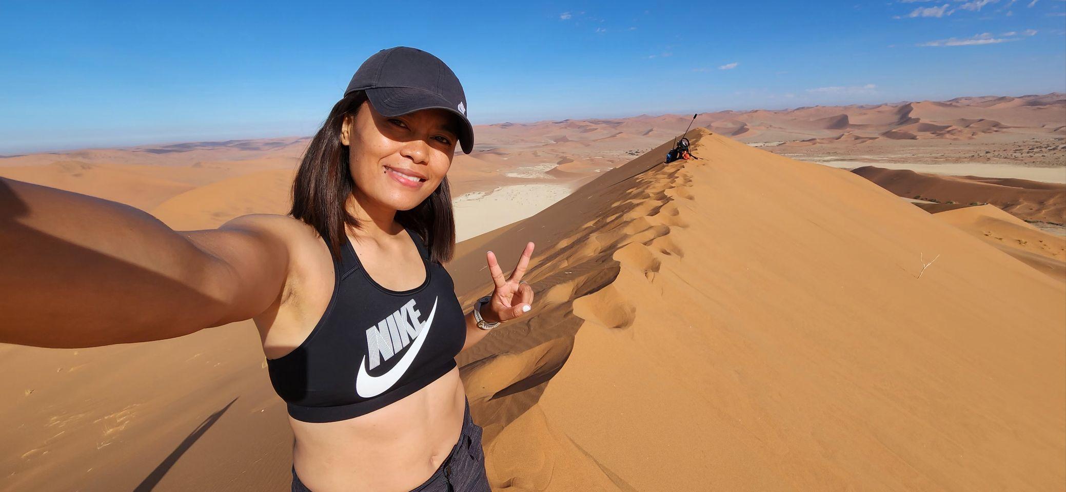 Max near the top of the ridge, Deadvlei's white pan visible far below, another figure still climbing behind her.