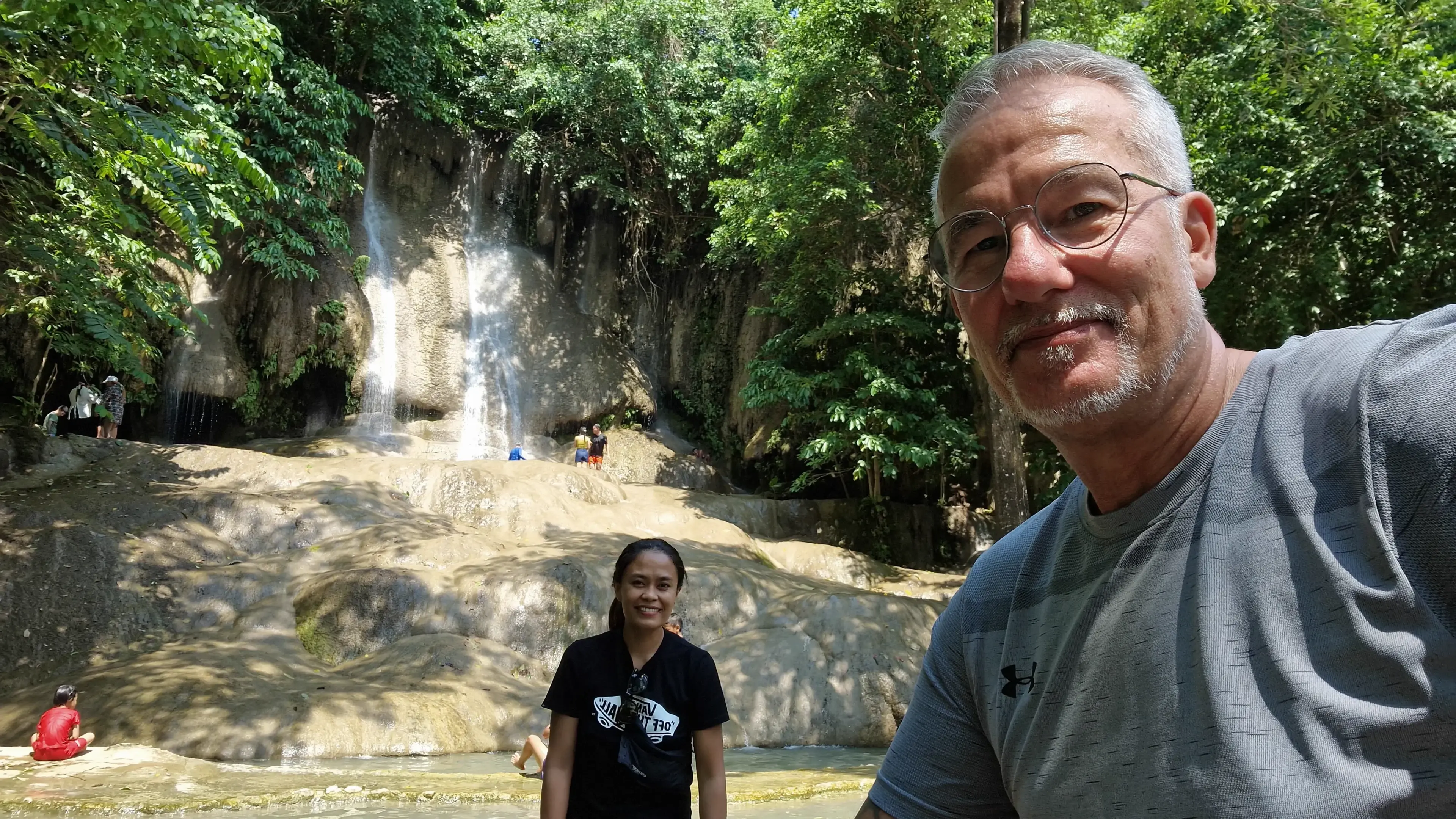 A small waterfall in a green, forested grotto, rock walls close on both sides.