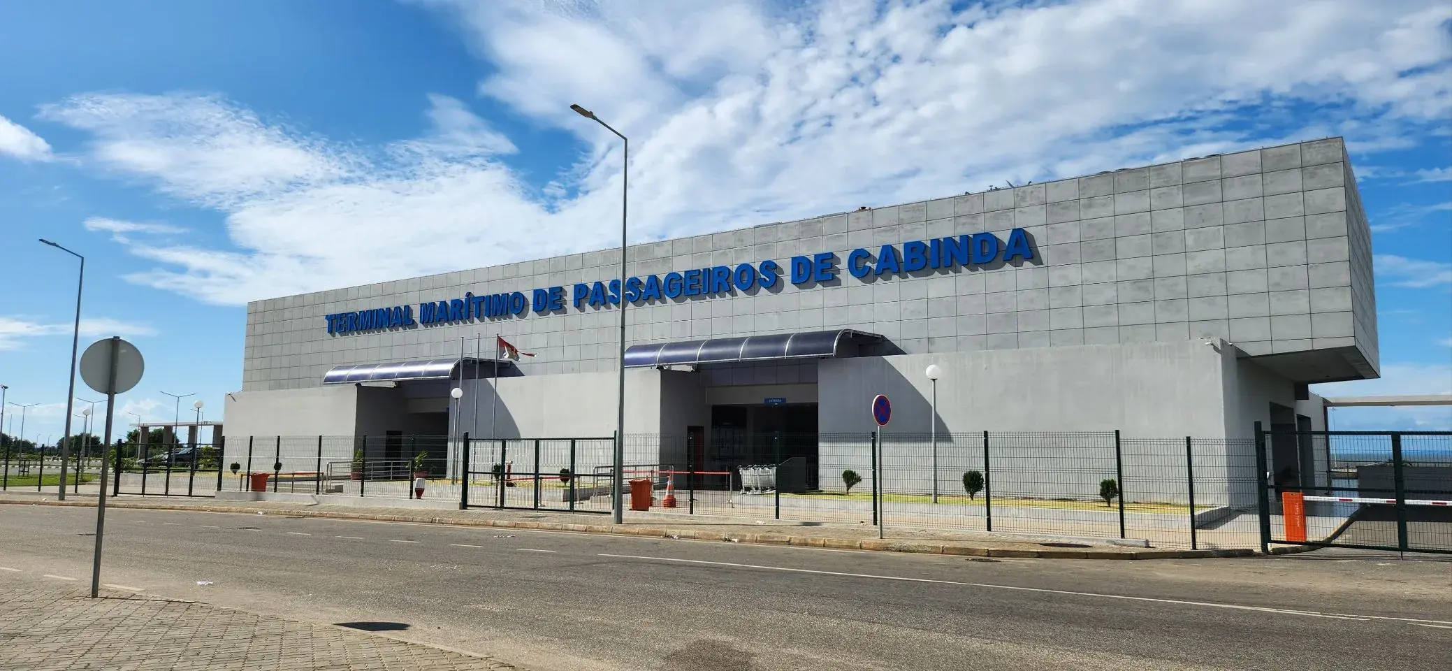 The Terminal Maritimo de Passageiros de Cabinda, a long grey concrete building with its name in tall blue letters, under a bright sky.
