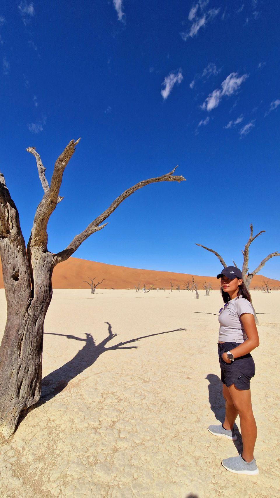 Max stands among Deadvlei's fossilised camel thorn trees, Big Daddy Dune rising behind her.