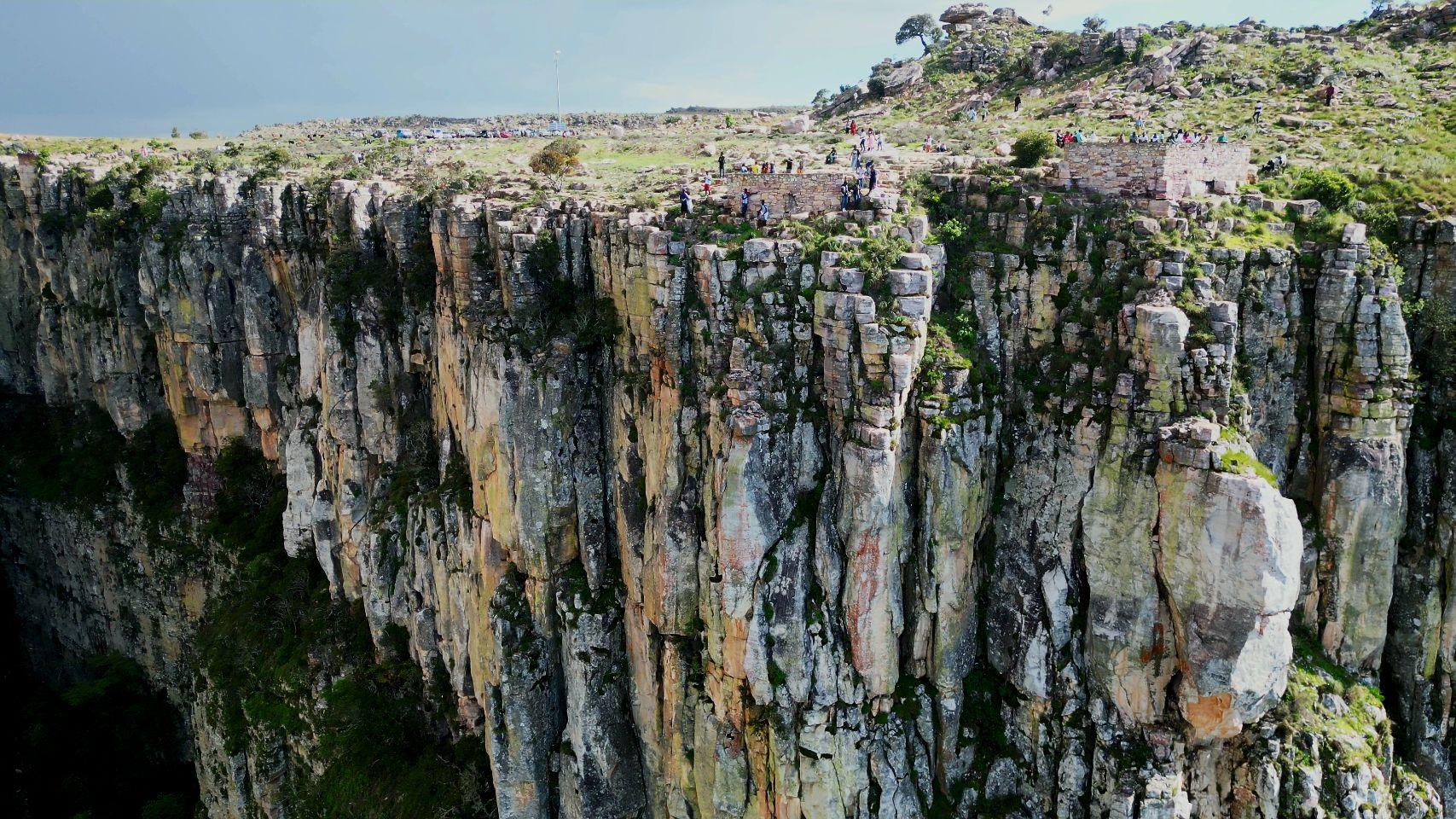 Sheer cliffs plunge into the Tundavala Gap in Angola, with a small crowd of visitors standing at the rim above.