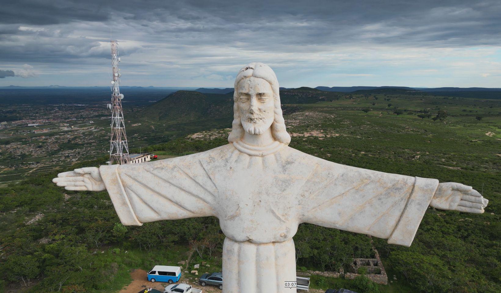 An enormous white statue of Christ with arms outstretched stands on a hilltop overlooking Lubango, Angola, seen from a drone.