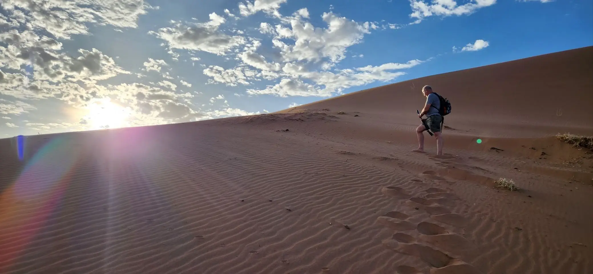 A person walking a knife-edge dune ridge in early morning light, sun flaring low over a long curved dune crest.